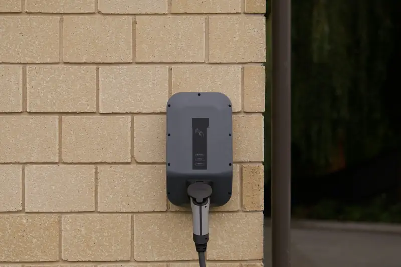 Une borne de recharge murale fixée sur un mur de briques claires, câble branché.